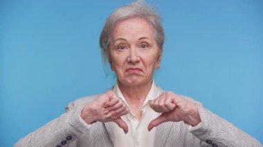 Yaşlı bir kadın her iki başparmağı aşağıda, hoşnutsuzluk, reddedilme ya da olumsuz görüş göstermek için kaşlarını çatıyor..