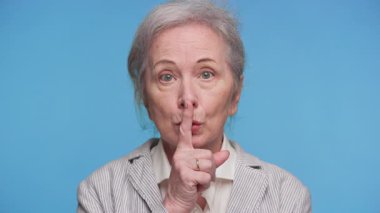 Dudaklarında parmakları olan yaşlı bir kadın, sessiz ol ya da bir sır tut diye işaret ediyor..
