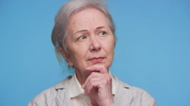 Gri saçlı, ceketli, düşünceli, çenesine dokunan, sağlık sigortası veya sigorta kararlarını düşünen yaşlı bir kadın..