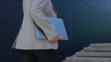 Üst katta elinde laptop olan spor ceketli profesyonel bir kadının fotoğrafı. İlerleme ve kararlılığı simgeliyor..