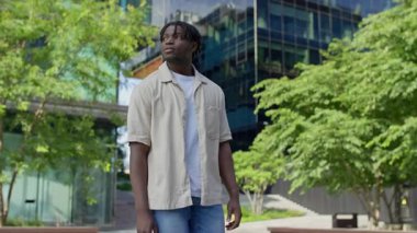 Çevresi yeşillik ve cam binalarla çevrili modern şehir parkında gezinen sıradan bir genç adam, huzurlu bir yaz gününün tadını çıkarıyor..