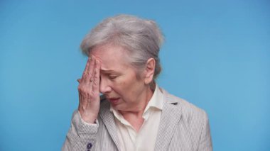 Alnını kapalı gözlerle rahatsız eden son sınıf öğrencisi kadın gözle görülür şekilde migren ya da mavi arka planda baş ağrısı çekiyor..