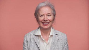 Çizgili ceketli neşeli yaşlı kadın pembe bir arka planda yumruk pompasıyla heyecan ve kendine güven gösteriyor..