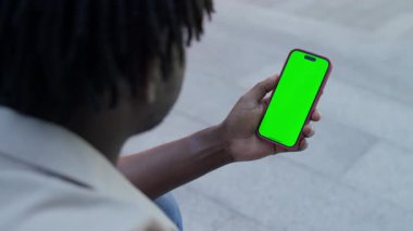 Boş yeşil ekranlı akıllı telefonu tutan bir adamın omuz üstü görünümü, model veya uygulama sunumu için ideal.