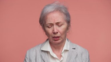 Pembe arka planda izole edilmiş, kötü ya da şok edici haberler aldıktan sonra üzgün ve üzgün bir şekilde elini ceketiyle yüzünü kapatan yaşlı kadın..