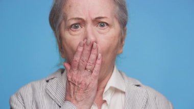 Şaşırmış, ağzı şoka girmiş yaşlı bir kadının, beklenmedik ya da üzücü haberlere tepki göstererek mavi arka planda kalması..