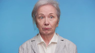 Şaşırmış bir yüz ifadesi olan yaşlı bir kadın, omuzlarını ve dudaklarını kaldırıyor..