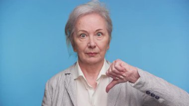 Sert görünüşlü son sınıf öğrencisi bir kadının mavi arka plana karşı hoşnutsuzluğunu ya da memnuniyetsizliğini ifade eden baş parmak işareti yapıyor..