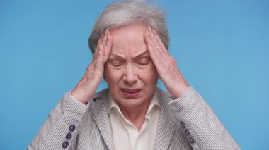 Görünür bir rahatsızlığı olan yaşlı bir kadın, gözleri kapalı ve elleri başının üstünde, baş ağrısından ya da stresinden şikayetçi..