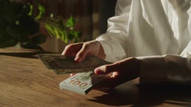 Yakın plan çekimde tahtadan bir masada 100 banknot sayılıyor, finans, servet, tasarruf veya ticari işlemleri temsil ediyor..