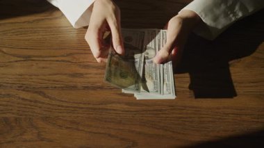 Tahta bir masanın üzerine 100 'er banknot yığıp dağıtan kişi, zenginlik, finans veya nakit akışını temsil ediyor..