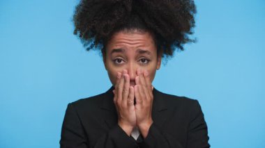 Ceketli bir kadının portresi. Şaşırmış ve endişeli görünüyordu. İki eliyle mavi arka planda ağzını kapatıyordu..