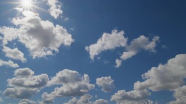Beyaz pofuduk bulutlar parlak mavi gökyüzünde güneş ışığıyla sürükleniyor, zaman diliminde ya da hareketli arka planlarda kullanılmak üzere yakalanıyor..