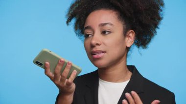 İş kıyafetleri içinde genç bir kadın akıllı telefonuyla konuşur, mavi arka planda hafifçe hareket ederken bir sesli mesaj kaydeder..