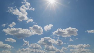 Pofuduk bulutlarla dolu mavi bir gökyüzünde parlayan parlak güneş, atmosferik hareketi yakalayarak zaman aşımına uğruyor..