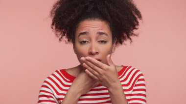 Çizgili gömlek giyen genç bir kadın boğazına acı dolu bir ifadeyle dokunuyor. Bu da pembe arka planda rahatsızlık veya ağrılı bir boğaz olduğunu gösteriyor..