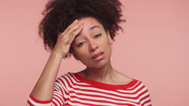 Çizgili gömlekli genç bir kadın iyi görünmüyor, alnını acı dolu bir ifadeyle tutuyor, yüksek ateş ya da yüksek ateş belirtileri gösteriyor..