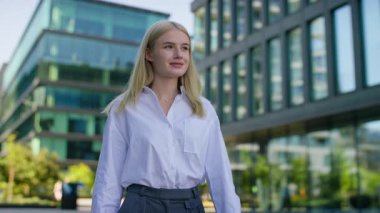 Modern ofis binalarının dışında yürüyen profesyonel genç bir kadın şehir iş ortamında güven ve hırs yayıyor..