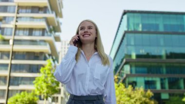 Gündüz vakti modern bir şehir iş bölgesinde yürürken telefonla konuşan kendinden emin genç bir kadın..