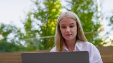 Yeşillik ve doğal ışıkla çevrili açık hava ortamında dizüstü bilgisayar kullanan konsantre genç bir kadının yakın çekimi..