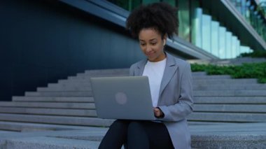 İş elbisesi giymiş düşünceli bir kadın dışarıda merdivenlerde otururken dizüstü bilgisayar kullanıyor kariyer seçimlerini ya da gelecek planlarını yansıtıyor..