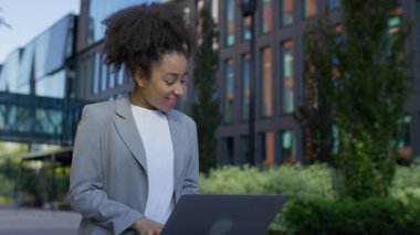 Spor ceketli mutlu genç bir kadın büyük bir gülümsemeyle dizüstü bilgisayarına bakıyor, olumlu haberlere ya da heyecan verici gelişmelere tepki veriyor..