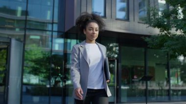 İş kıyafetleri içinde kendinden emin genç bir kadın, sabah işe gidip gelirken elinde bir dizüstü bilgisayarla modern bir ofis binasının önünde yürüyor..