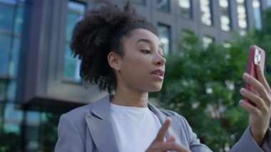 Kendine güveni tam bir iş kadını, modern bir şehir bölgesinde, açık havada yürürken, akıllı telefonuyla birden fazla iş yapıyor ve iletişim kuruyor..