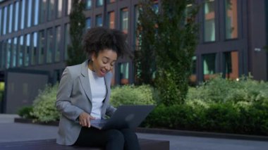 Modern ofis binasının önünde duran mutlu iş kadını, bir hedefe ulaştıktan ya da dizüstü bilgisayardan iyi haberler aldıktan sonra kutlama için yumruklarını kaldırıyor..