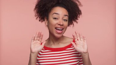 Mutlu genç bir kadın gülümsüyor ve iki eliyle pembe bir arka plana el sallıyor, kırmızı ve beyaz çizgili bir gömlek giyiyor, dostça bir veda ve pozitifliği ifade ediyor..