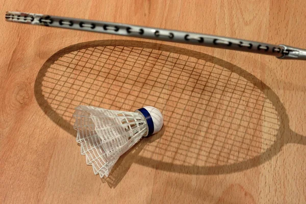 The rocket casts a shadow on the shuttlecock lying on the floor. Badminton game. Rocket shadow.