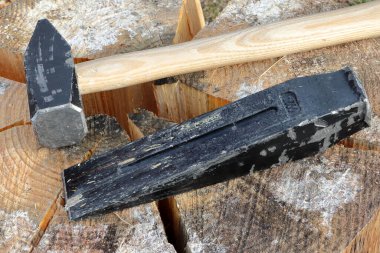 An iron wedge and a hammer are placed on a split wooden log. Preparation of firewood. A pine log cut in half. 