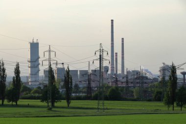 Ön planda saf yeşil doğa, arka planda sisli bir fabrika. Ağır sanayi, hava kirliliği. Yeşil Anlaşma.