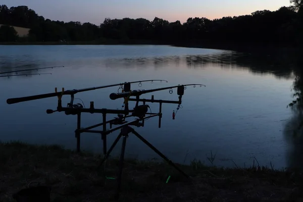 The sun setting over the horizon and fishing by the pond. Stand with fishing rods. The surface of the lake.