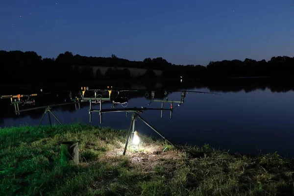 Night photo fishing by the pond. Stand with illuminated fishing rods. The sky with stars, the surface of the lake.