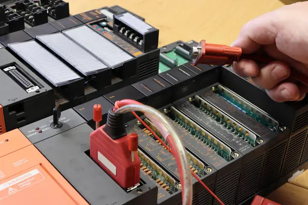 Bir el, PLC 'ye bir iletişim kablosu tutuyor. Programlanabilir mantık denetleyicisi. Bağlayıcıya odaklanmış. Kablo bağlantısı detayı. Endüstriyel kontrol sisteminin test ve programlanması.