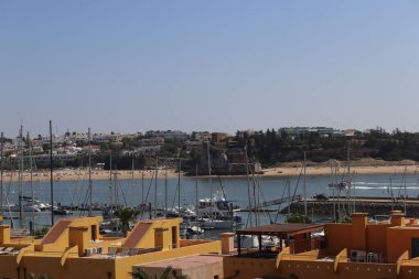 Portekiz 'in güneşli Algarve bölgesindeki Portimao' dan çekilen Ferragudo kıyı şeridinin çarpıcı panoramik manzarası. Resimde, Ferragudo 'nun büyüleyici köyü üzerinde tünemiş çeşitli tekne ve yatlarla benekli huzurlu koy sergileniyor.