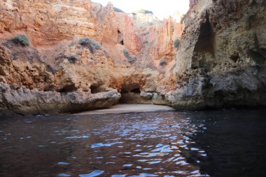 Portekiz 'in Portimao yakınlarındaki gizli bir deniz mağarası ile Algarve sahil şeridinin nefes kesici güzelliğini keşfedin. Görüntü dramatik, katmanlı kaya oluşumlarını sergiliyor. Sıcak, dünyevi tonlarda. Huzurlu bir şekilde yükseliyor.