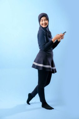 Siyah etek ve siyah pantolon giyen bir kadın cep telefonu tutuyor. Gülümsüyor ve mutlu.