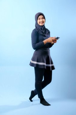 Siyah etek ve siyah pantolon giyen bir kadın cep telefonu tutuyor. Gülümsüyor ve mutlu.