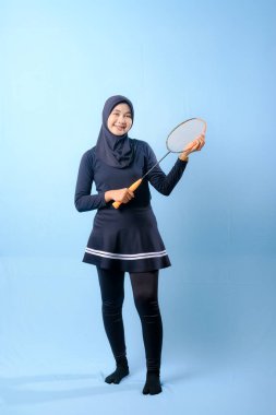 Siyah etekli ve elinde badminton raketi olan siyah pantolonlu bir kadın. Gülümsüyor ve mutlu.