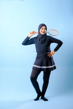 Siyah etekli ve elinde badminton raketi olan siyah pantolonlu bir kadın. Gülümsüyor ve mutlu.