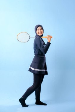 Siyah etekli ve elinde badminton raketi olan siyah pantolonlu bir kadın. Gülümsüyor ve mutlu.