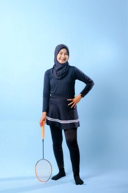 Siyah etekli ve elinde badminton raketi olan siyah pantolonlu bir kadın. Gülümsüyor ve mutlu.