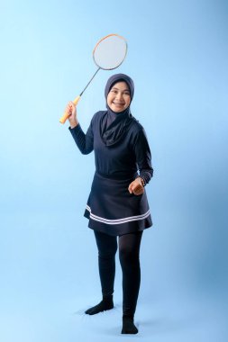 Siyah etekli ve elinde badminton raketi olan siyah pantolonlu bir kadın. Gülümsüyor ve mutlu.