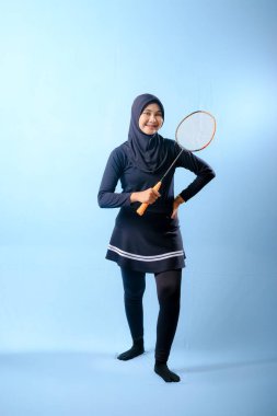 Siyah etekli ve elinde badminton raketi olan siyah pantolonlu bir kadın. Gülümsüyor ve mutlu.