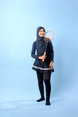 Siyah etekli ve elinde badminton raketi olan siyah pantolonlu bir kadın. Gülümsüyor ve mutlu.