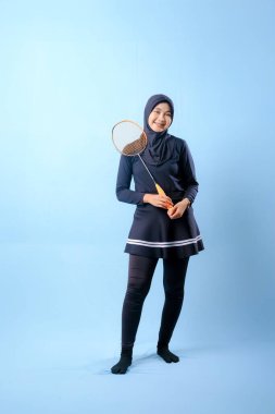 Siyah etekli ve elinde badminton raketi olan siyah pantolonlu bir kadın. Gülümsüyor ve mutlu.