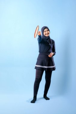 Siyah etekli ve elinde badminton raketi olan siyah pantolonlu bir kadın. Gülümsüyor ve mutlu.