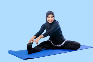 Bir kadın laptopu ve su şişesi olan bir minderde yoga yapıyor. Gülümsüyor ve antrenmanından zevk alıyor.